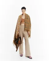 Manta de tejido grueso con flecos en los bordes, color mostaza y gris, con diseño de monograma repetitivo.