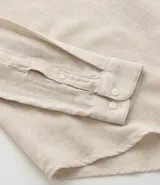 Camisa blanca de manga larga, corte amplio y cuello padre (mandarín). Presenta un frente abotonado con tapeta corta.