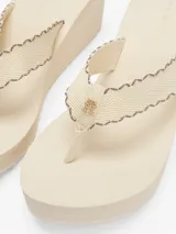 Ojotas color crema con plataforma tipo cuña, tiras tejidas con ribete a contraste y monograma TH en la tira del dedo.