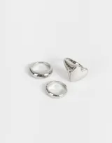 Set de tres anillos dorados de metal con diferentes diseños: uno liso, uno con forma de corazón y uno con forma de domo.