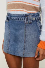 Minifalda de jean azul con tiro medio y detalles de apliques estilo cinturón en la cintura. Tiene cuatro pasacintos anchos en la delantera y dos bolsillos en la parte posterior.