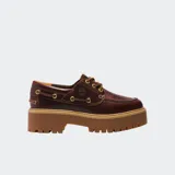 Zapato tipo náutico de cuero color marrón oscuro, con cordones y ojales metálicos dorados. Presenta una suela plataforma gruesa y dentada de color caramelo.