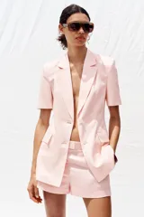 Blazer color rosa confeccionada en lino, con cuello solapa, manga corta con hombreras, bolsillos delanteros con solapa, cintura entallada y cierre frontal con botones.