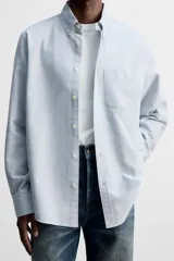 Camisa celeste a rayas verticales, de corte regular fit, confeccionada en tejido de algodón. Tiene cuello abotonado, manga larga con puños abotonados, bolsillo de parche en el pecho y cierre frontal con botones.