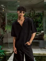 Camisa de manga corta color crudo/blanco, confeccionada en tejido de punto abierto con textura calada y cuello polo. Presenta cierre frontal de botones.