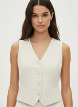 Chaleco sastrero color beige claro, de corte entallado, con escote en V y cierre frontal de botones. Presenta bolsillos falsos con pespunte en la parte inferior delantera.