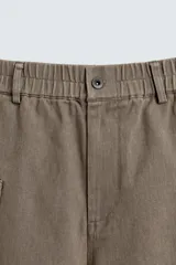 Pantalón cargo de algodón color marrón con efecto lavado, corte relajado y tiro medio. Presenta cintura elástica con botón y cierre de cremallera, bolsillos delanteros, bolsillos plastrón en la espalda y grandes bolsillos cargo en las perneras.