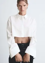 Camisa blanca de popelina de algodón y lyocell, corte crop, manga larga con puños abotonados, cuello camisero y cierre frontal con botones ocultos.