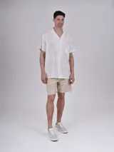 Camisa de manga corta con estampado de hojas color verde sobre fondo beige, cuello solapa y bolsillo en el pecho.