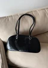 Cartera tipo baguette de cuero sintético color negro con doble asa corta y cierre superior con cremallera.