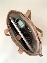 Cartera tipo tote de cuero graneado color negro, con textura uniforme y suave al tacto. Tiene manijas de 55 cm, bolsillo frontal con broche imantado, bolsillo trasero con cierre metálico, cierre principal metálico, forro interior y tres bolsillos internos (uno con cierre, uno plaqué y uno tipo sobre con solapa y botón).