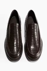 Mocasines marrones con textura de piel de cocodrilo, costura tradicional en la parte delantera, forro de lona de algodón y suela de goma. Tacón de 1 cm.