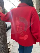 Camisa roja tejida en lana con cuello clásico, manga larga y cierre frontal con botones. Tiene un bolsillo de parche en el pecho con detalle de cuero.