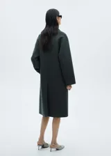 Abrigo largo verde oscuro de doble botonadura con solapas de muesca, hombros caídos y bolsillos laterales.