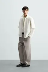 Pantalón de vestir color blanco hueso, de corte recto y tiro medio, con cintura elástica y cierre frontal de botón y cremallera. Presenta bolsillos frontales y bolsillos traseros de vivo.