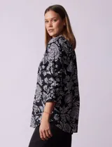 Blusa negra con estampado floral blanco, cuello mao con escote en V y abertura frontal con botones. Manga 3/4 con terminación fruncida.