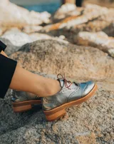 Zapato acordonado color bronce de cuero vacuno con perforaciones decorativas, taco de madera con folia en cuero de 4cm y entre suela de goma de 1,5cm. Horma de punta redonda y cómoda.