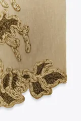 Chaleco color arena con bordados florales en hilo dorado y cuentas negras.