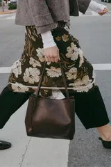 Bolso de hombro tipo shopper de cuero sintético color marrón oscuro, con pespuntes decorativos en el cuerpo y asas delgadas. Cierre principal con botón imantado y bolsillo interior con cremallera.