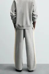 Pantalón de jogging gris con corte relaxed fit, cintura elástica ajustable con cordón interior, bolsillos laterales y traseros de vivo, y banda lateral color crema.
