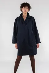 Gabardina azul marino de largo medio y corte recto, fabricada en nailon repelente al agua. Presenta cuello solapa, cierre frontal con botones ocultos, mangas largas con puños anchos y bolsillos laterales inclinados.
