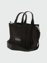Bolso tote pequeño de lona color beige con estampado frontal en blanco con la leyenda "The Tote Bag Marc Jacobs". Tiene doble asa de mano y correa bandolera negra ajustable y extraíble.