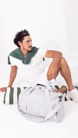 Bolso deportivo gris de nylon con doble asa y correa regulable. Cuenta con dos bolsillos exteriores con cierre, un bolsillo exterior de rejilla y un bolsillo interior con cierre.