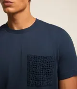 Remera azul marino de algodón, con cuello redondo y manga corta. Presenta un bolsillo delantero con detalles bordados.