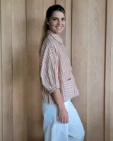 Camisa color beige con rayas verticales blancas, cuello clásico, mangas 3/4 y bolsillos frontales cuadrados.