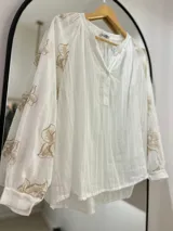 Blusa blanca con escote en pico y botones en el frente. Detalles florales bordados en mangas.