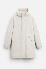Parka color crudo de tejido técnico acolchado, con cuello alto y capucha ajustable. Tiene mangas largas con puños ajustables, bolsillos frontales con solapa, bolsillo interior y cierre frontal con cremallera oculta y botones a presión.