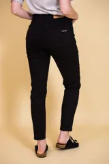 Pantalón jean negro de tiro alto, con cinco bolsillos, confeccionado en tela con elastano. Tiene cierre frontal con doble botón y cierre metálico, y detalle de cuero en la parte delantera de la pretina.