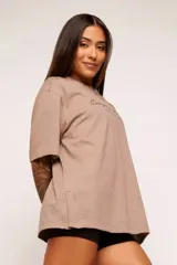 Remera color beige con estampado de texto en el frente, corte amplio y mangas cortas.