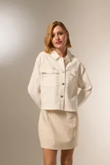 Chaqueta corta de jean color crudo, con cuello camisero, cierre frontal con botones metálicos y bolsillos de parche en el pecho con tachas metálicas.