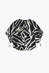 Top de cuello redondo y escote pico con estampado animal print cebra en blanco y negro. Manga corta abullonada ajustable con lazadas.