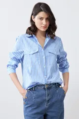 Camisa celeste con rayas verticales blancas, de manga larga y corte clásico, con cuello camisero y dos bolsillos con solapa en el pecho.