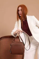 Bandolera de cuero sintético color beige, con diseño compacto y elegante. Cuenta con un bolsillo frontal con cierre y un compartimento principal con cierre. La correa es regulable.