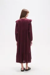 Vestido midi holgado de viscosa color vino tinto, con mangas largas y volados en los hombros. Presenta un canesú con bordado floral en tonos rosados y cuello con abertura en forma de lágrima y lazo para atar.