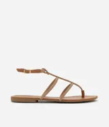 Sandalias planas tipo gladiadoras color tostado, con tiras finas con strass, punta redonda y cierre con hebilla en el tobillo.