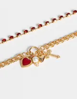 Set de dos collares dorados con cadenas de diferentes diseños. Uno con strass rojos y otro con dijes de corazón, perla y cruz.