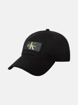 Gorra de béisbol negra de algodón tipo sarga, con visera curva y cierre ajustable con hebilla. Presenta un parche rectangular de silicona en el frente con el logo de Calvin Klein en color verde lima.