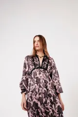 Vestido largo rosado con estampado floral negro, escote en V con ribete negro, mangas largas abullonadas y falda escalonada con volantes.