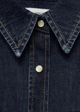 Camisa de denim azul oscuro con cuello camisero, cierre frontal con botones a presión, dos bolsillos con solapa abotonada en el pecho y mangas largas con puños abotonados. Incluye bolo tie con dije plateado y turquesa.