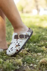 Zueco con capellada de pelo de vaca con manchas marrones y negras sobre base blanca, plantilla anatómica de cuero y hebilla lateral ajustable.