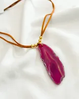 Collar con dije de piedra ágata fucsia irregular, engarzada con cuentas doradas y colgante de cordón marrón.
