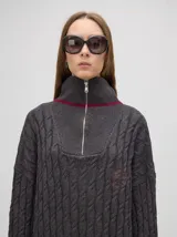 Buzo de algodón tejido en ochos, color gris, con cuello alto con cierre de cremallera hasta arriba, puños a rayas de colores y caída por debajo de la cadera.