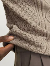 Sweater de punto color beige con cuello alto y cierre de cremallera parcial.