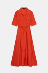 Vestido midi camisero color ladrillo, confeccionado en popelina de algodón. Presenta cuello solapa, manga corta con puños abotonados, bolsillos laterales ocultos y bolsillos de parche con solapa en el pecho. Incluye cinturón lazada en el mismo tejido y cierre frontal con botones ocultos.