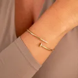 Brazalete rígido abierto en oro amarillo 18k con forma de clavo y detalles de circonias.