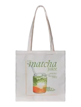 Bolso tote de tela color crudo con asas largas, estampado frontal de un vaso de bebida en capas (matcha, naranja) con pajita, y texto relacionado con matcha juice.